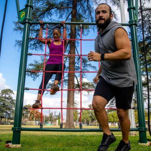 A woman climbing the Cargo Net & Rope Climb and a man running away from it