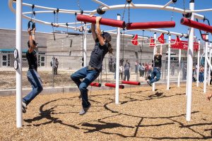 One teen boy hanging from the Spider Walk and another hanging from rings on an X-Treme Ninja Course