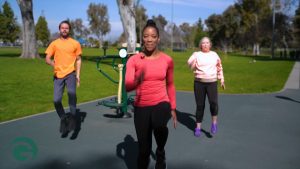 Two women and a man stepping in place in front of 4-Person Pendulum, Abs & Dips Station