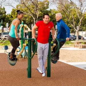 Two men and a woman using the 4-Person Pendulum, Abs & Dips Station